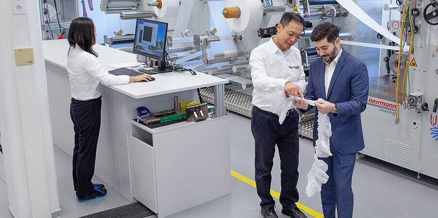 Staff inspecting nonwoven material at a machine in a technical laboratory